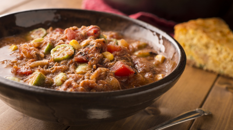 Bowl of Brunswick stew with slice of cornbread in the background