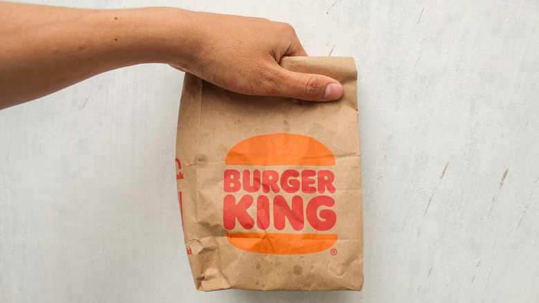 A hand holds up a Burger King restaurant bag