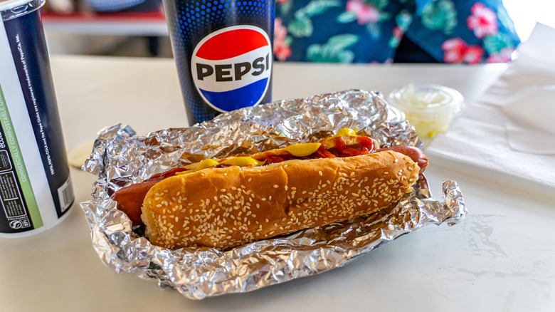 A Costco hot dog in a foil wrapper with a drink