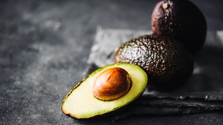 half of an avocado and two whole avocados on slate
