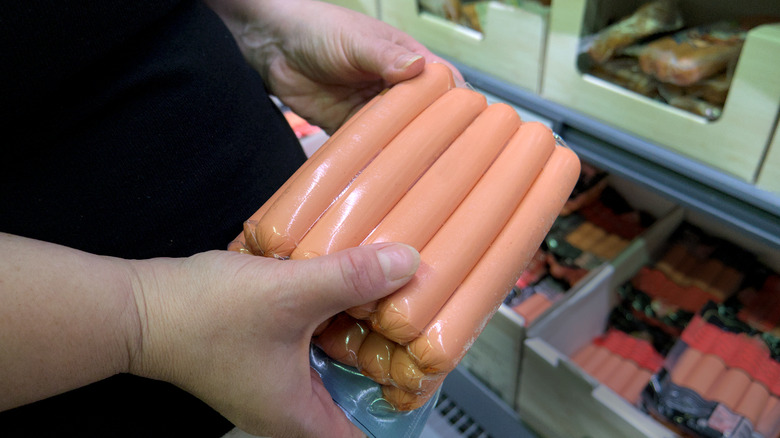 A woman holds a package of hot dogs in a grocery store