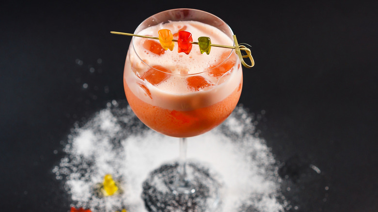 A cocktail in a stem glass garnished with a trio of gummy bear candies