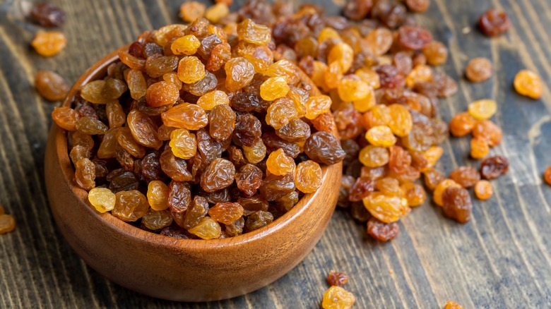 raisins in a bowl and scattered on a wood table