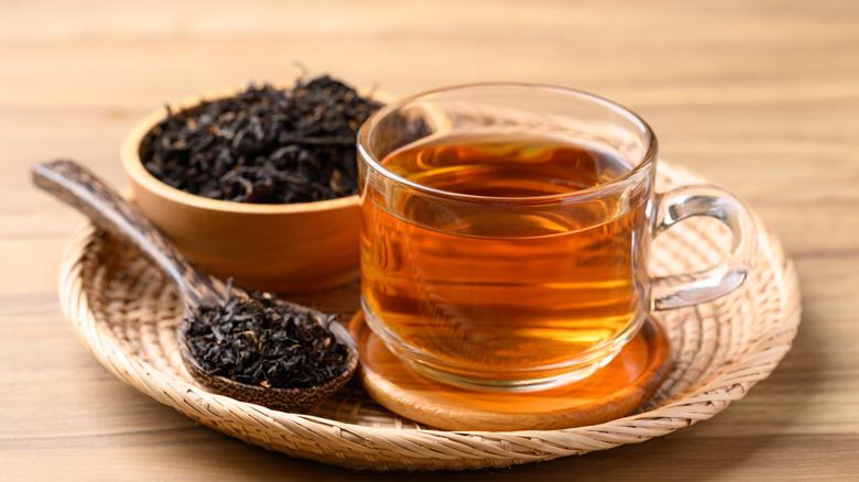 A glass cup of tea next to a bowl and spoon of full-leaf tea