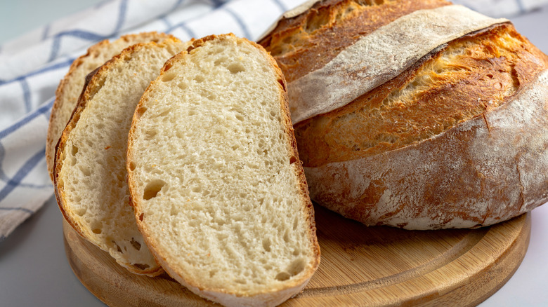 Baked loaf of sourdough bread with sliced sourdough pieces on wooden tray