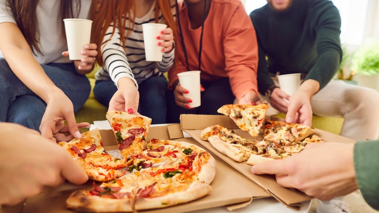 Friends eating pizza and holding cups