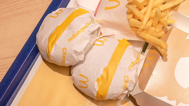 Two McDonald's cheeseburgers in wrappers with fries