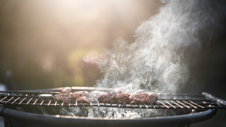 Charcoal grill with heavy smoke rising off meat