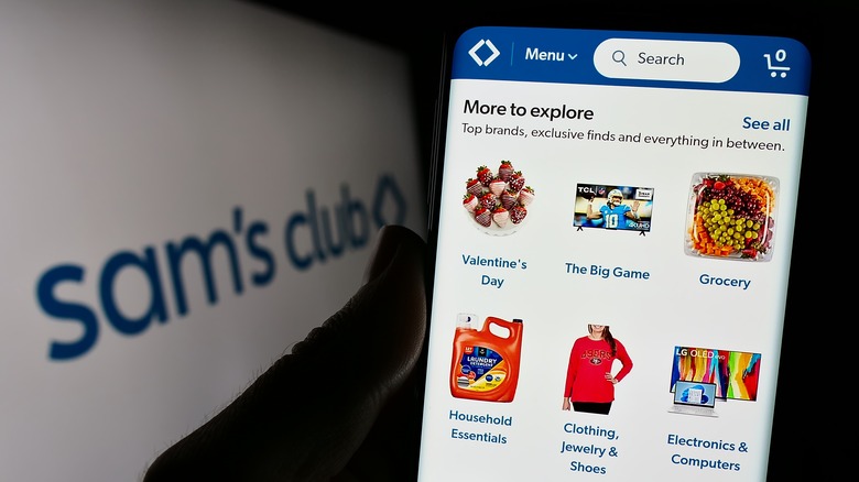 A darkened hand holds a phone with the Sam's Club app open on the screen