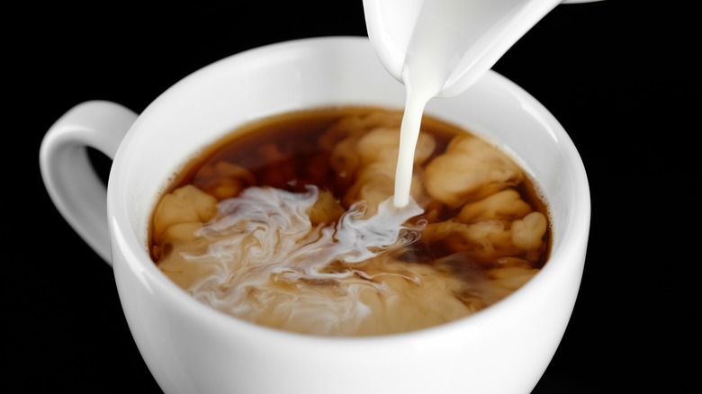 coffee creamer being poured into cup of coffee