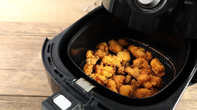 A black air fryer basket full of breaded, fried chicken pieces