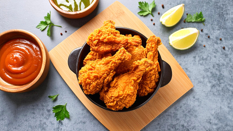 Golden brown fried chicken next to ketchup and limes