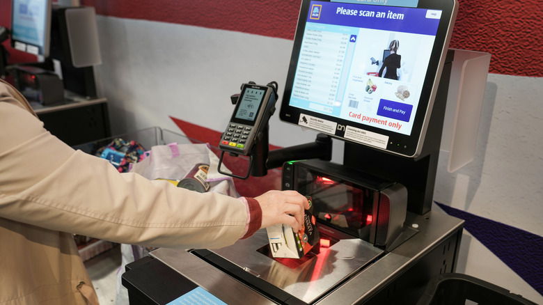 A woman scans an item at an Aldi self-checkout kiosk