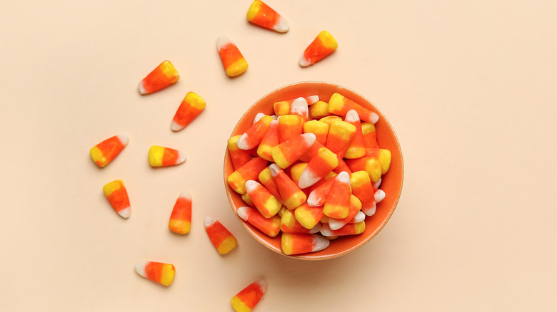Candy corn in a bowl on a pink background with candy corns scattered around.