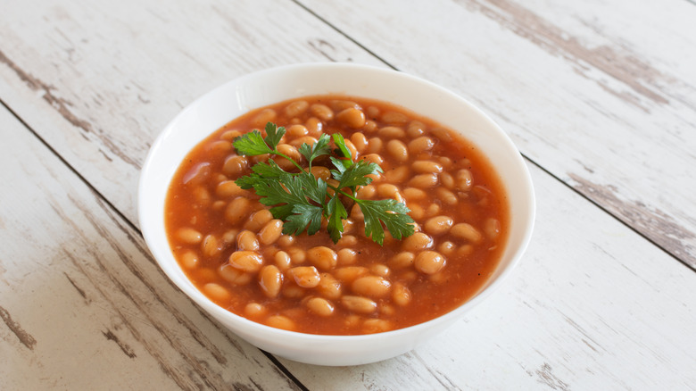 A bowl of baked beans with a sprig of fresh parsley in the center.