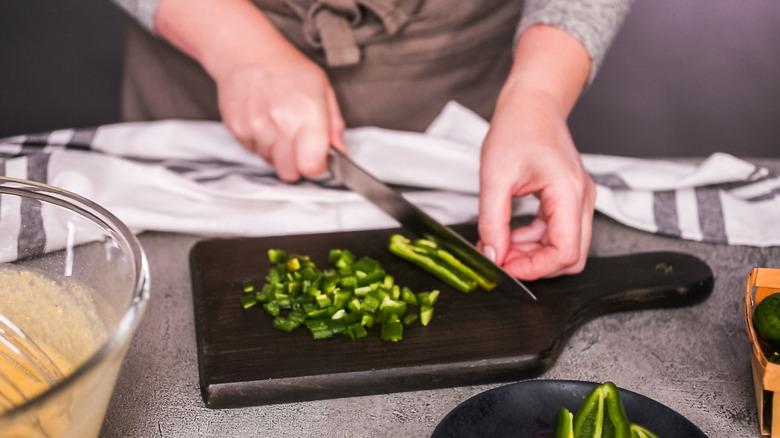 A person uses a knife to dice a fresh jalapeno