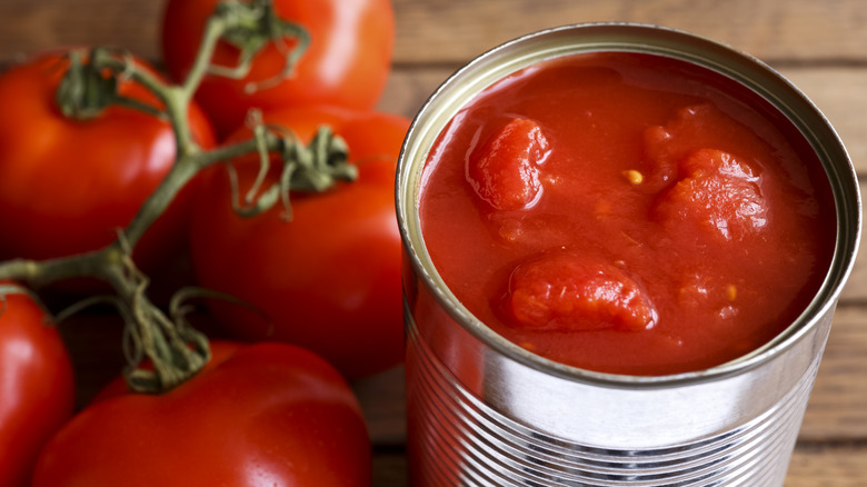 An open can of tomatoes next to fresh tomatoes