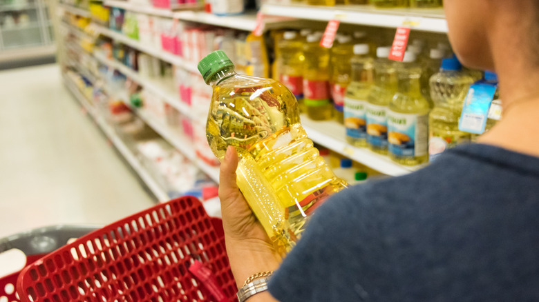 A woman holds a bottle of unlabeled oil in a supermarket