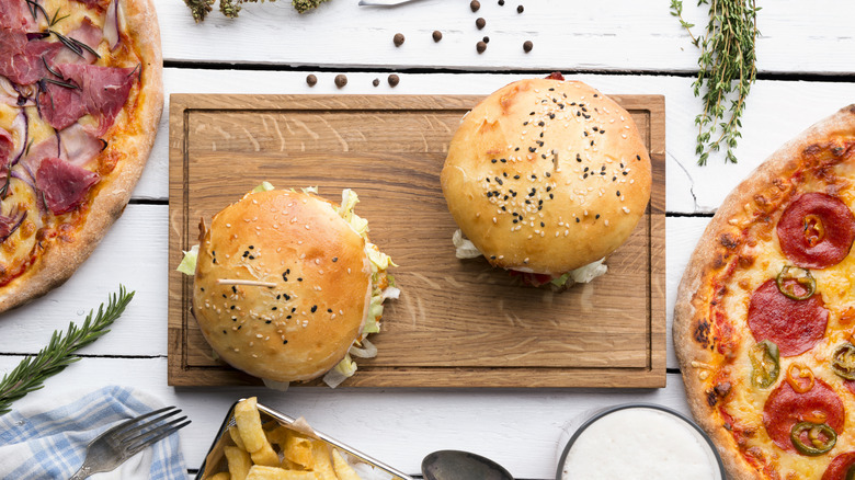Two burgers and two pizzas on a wooden table