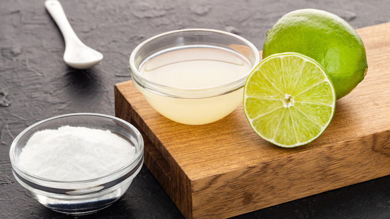 Limes sit next to two small bowls filled with lime juice and baking soda