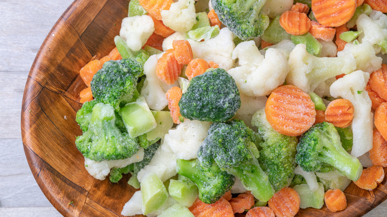 A wooden bowl contains a frozen vegetable medley of broccoli, sliced carrots, and cauliflower