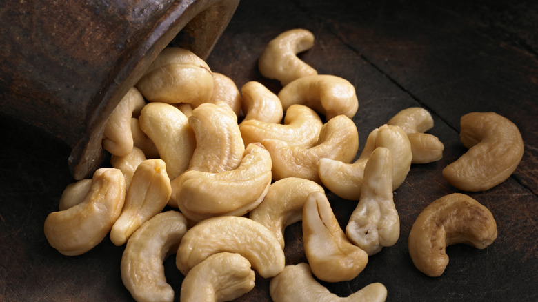 whole cashews spilling out of a jar onto a wooden surface