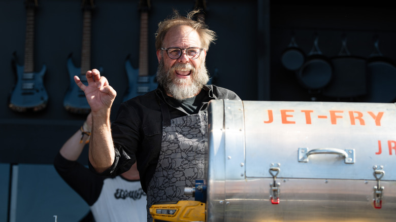 Chef Alton Brown stands next to a food smoker at a cooking demonstration