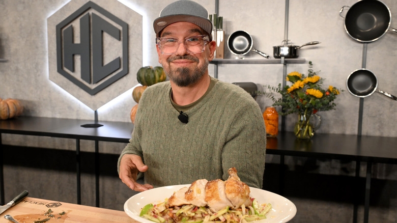 Chef Michael Symon holds a plate of veggies and roasted chicken in a studio kitchen