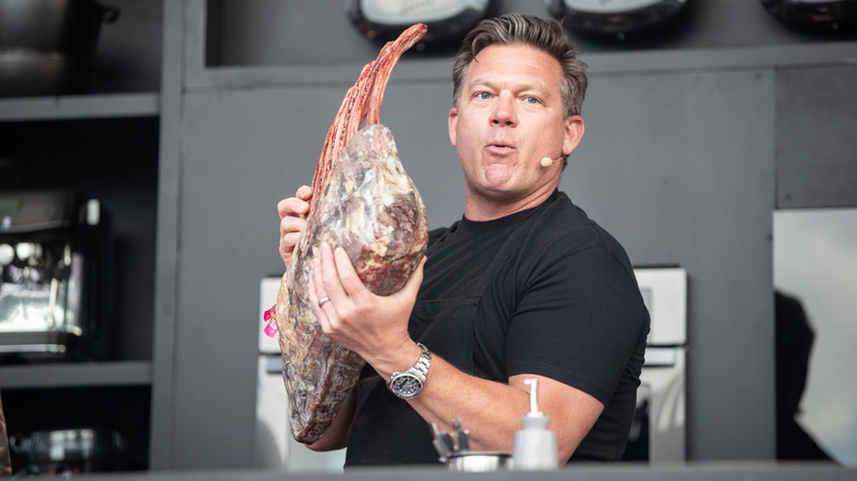 Chef Tyler Florence holds an oversized rack of ribs at an outdoor cooking demonstration