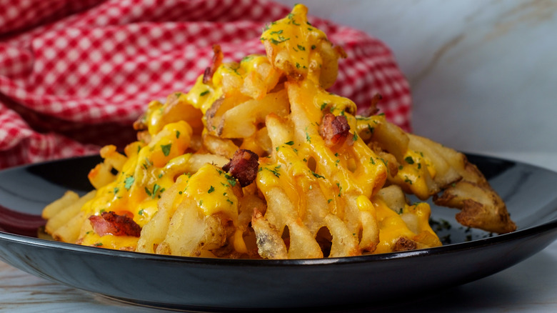 Plate of waffle fries topped with cheese and bacon