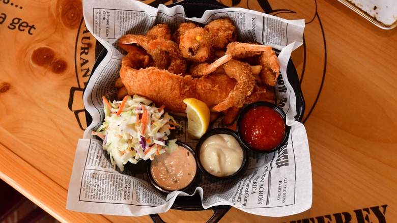 Bubba Grump Shrimp Co.'s Forrest's Seafood Feast with fried fish, shrimp, and hushpuppies visible with coleslaw, cocktail sauce, remoulade sauce, and tartar sauce.