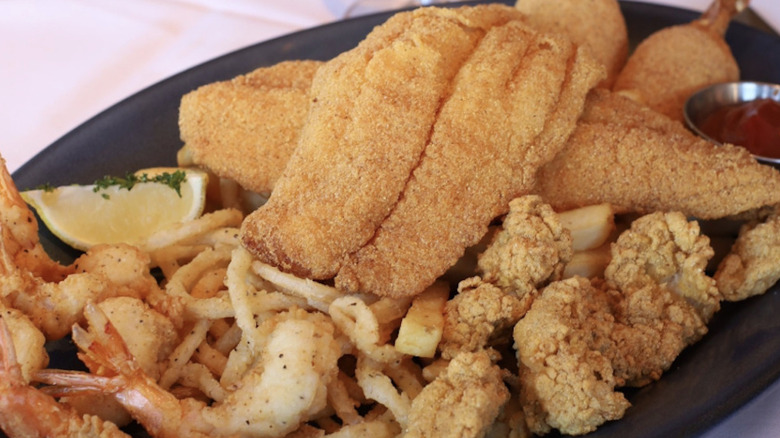 Landry's Seafood House Fried Seafood Platter with fried fish, shrimp, fries,and onion rings with lemon and ketchup on the side.