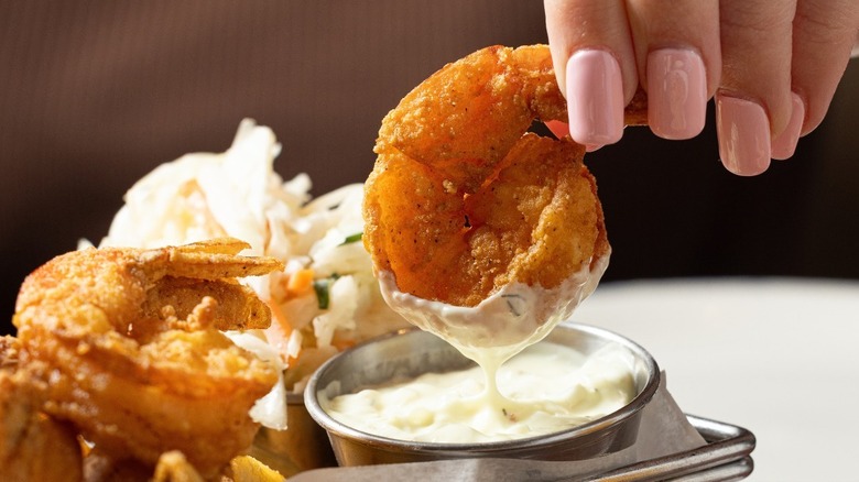 Someone dipping fried shrimp in tartar sauce from Legal Sea Foods