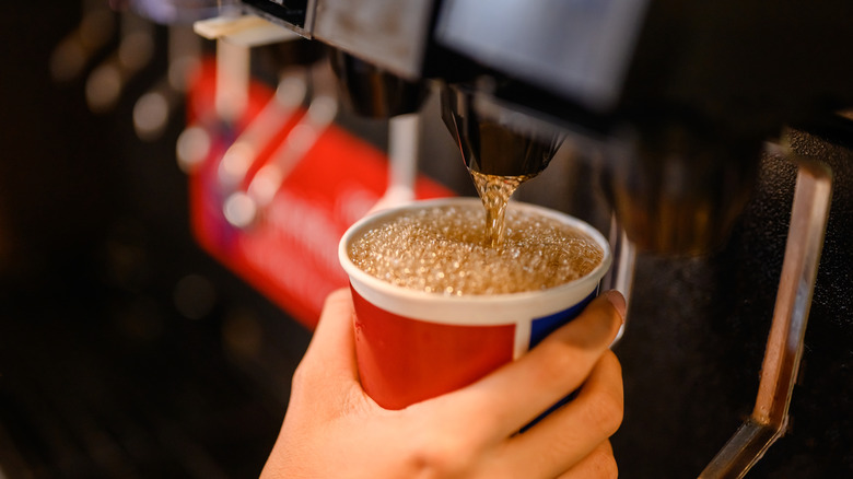 Close-up of a hand holding a cup while dispensing soda from a fast food soda machine