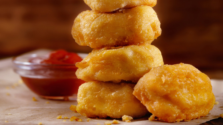 Close-up of a a stack of chicken nuggets beside a glass bowl of ketchup