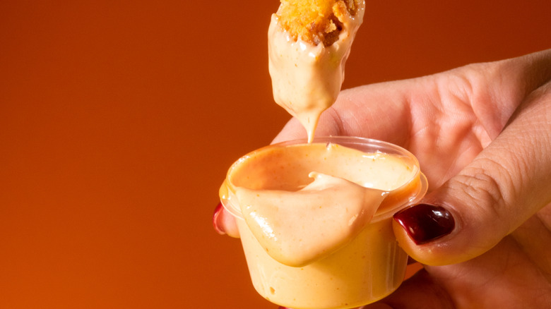Close-up of a woman dipping a chicken tender into a small container of sauce