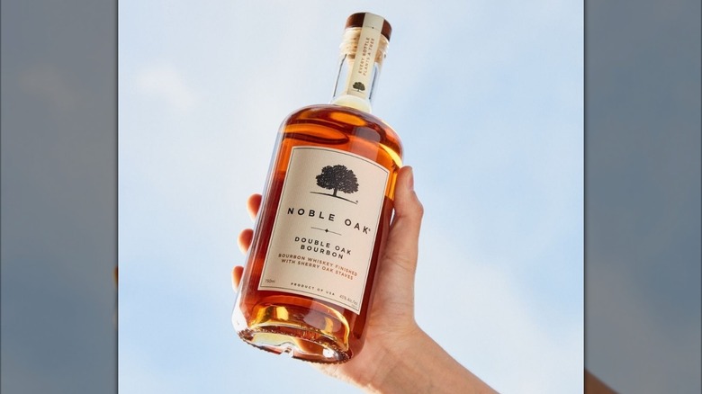 Hand holding bottle of Noble Oak bourbon