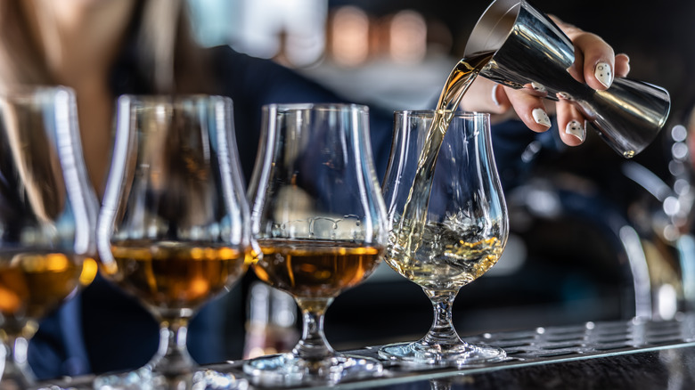 Four gasses of whiskey and a hand pouring whiskey into the last one