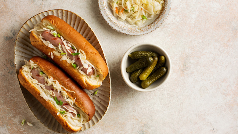 Two hot dogs on a plate topped with pcikled cabbage
