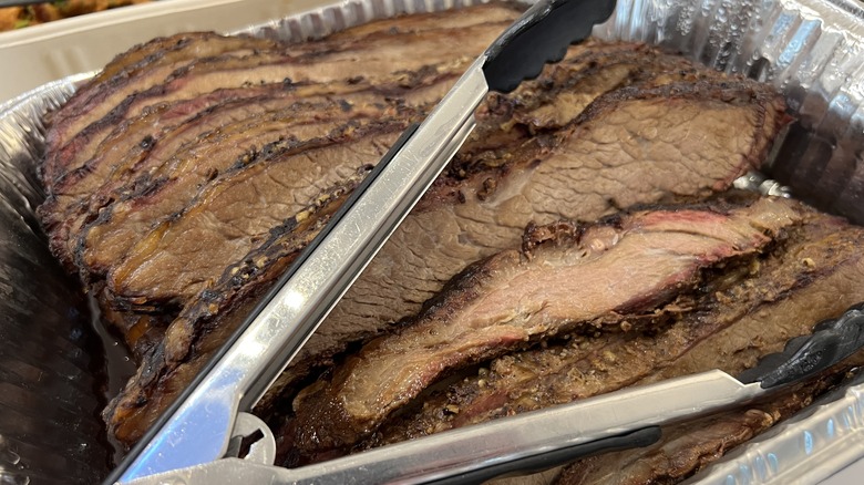 foil container of sliced brisket and serving tongs