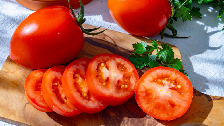 Whole and sliced roma tomatoes on a wooden cutting board.