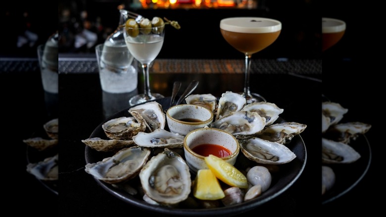 A plate of oysters and two drinks in the background.