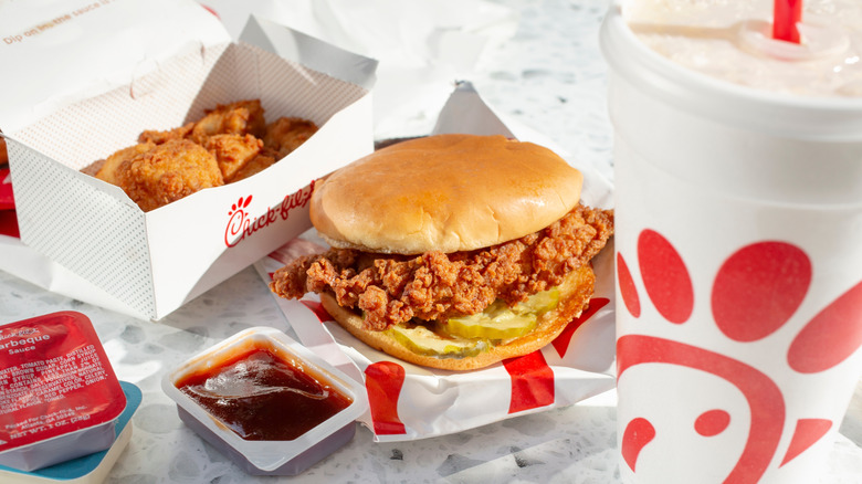 A Chick-fil-A chicken sandwich with sauce, nuggets, and a drink.