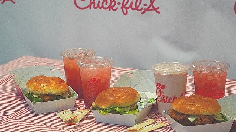 Side angle of Chick-fil-A Jalapeño Club Chicken Sandwiches, Jalapeño Ranch sauce packets, and Strawberry Hibiscus Beverages.