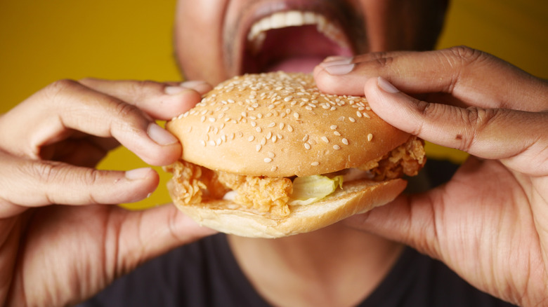 A black man prepares to take a bite of a chicken sandwich held between his hands.