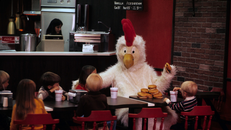 Doodles, the very first Chick-fil-A mascot, sits at a restaurant table with young customers