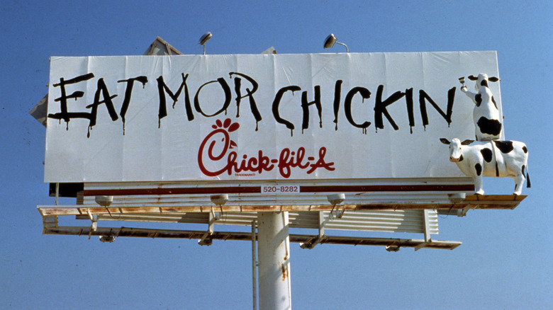 A Chick-fil-A billboard shows the chain's cow mascots painting "Eat Mor Chickin" on the sign