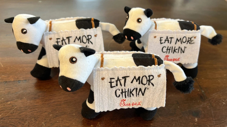 Three plush Chick-fil-A cow collectibles wearing "Eat Mor Chikin" signs