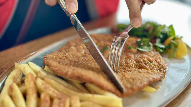 Cutting up schnitzel with fries and salad