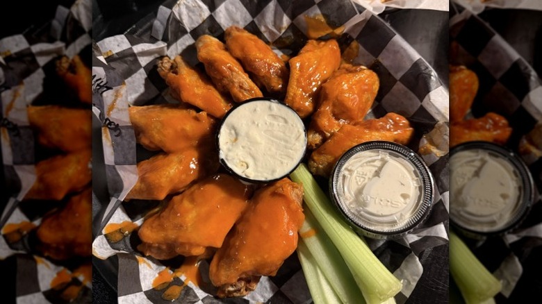 Buffalo chicken wings from Bar Bill Tavern sit in a paper covered tray with celery and dips